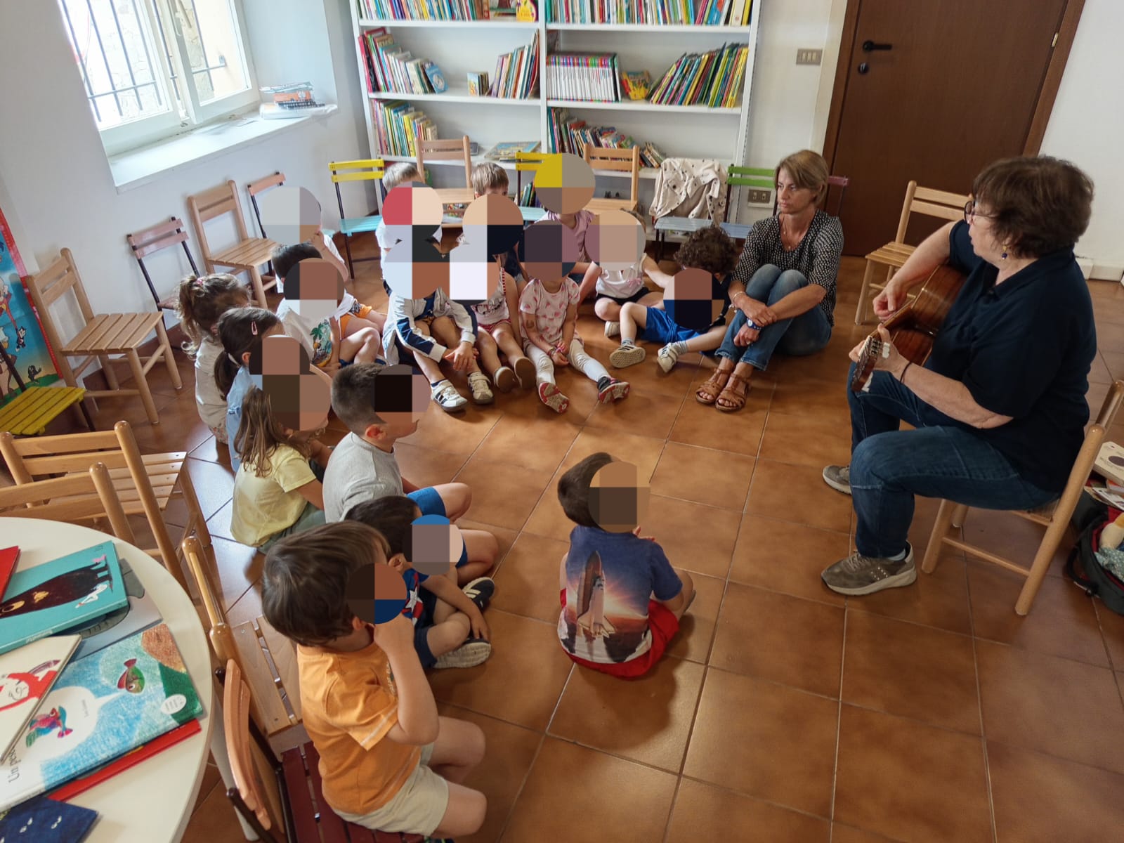 Bambini seduti per terra in cerchio che ascoltano un adulto che suona la chitarra